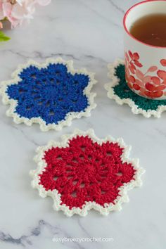 three crocheted coasters sitting on top of a marble counter next to a cup of tea