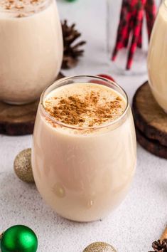 two glasses of eggnog with cinnamon on the rim and christmas decorations in the background