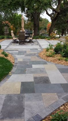 a stone walkway in the middle of a park with trees and lawn furniture on it