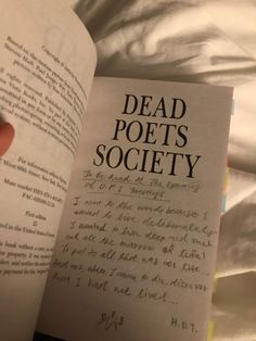 a hand holding an open book in front of a white sheet with the words dead poets society written on it