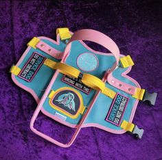 a pink and blue bag with yellow straps sitting on top of purple velvet covered ground