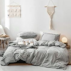 a bed with grey sheets and pillows in a white room next to a table lamp