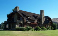 a large stone house with two chimneys on the front and one in the back, surrounded by lush green grass