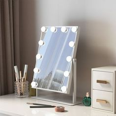 a white vanity mirror sitting on top of a table next to a drawer with pens and pencils