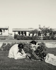 two women sitting on the grass in front of a building