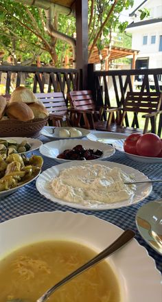 a table topped with plates of food next to bowls of soup and bread on top of a blue checkered table cloth