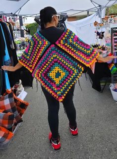 a woman is walking down the street carrying a colorful crocheted granny shawl