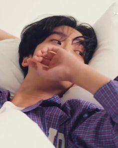 a young man laying in bed with his hand on the pillow and making a funny face