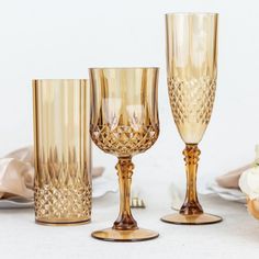 three gold colored wine glasses sitting next to each other on a white tablecloth covered table