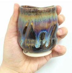 a hand holding a small ceramic vase in it's left hand, with multiple colors on the outside