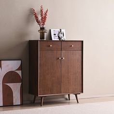 a wooden cabinet sitting next to a painting on the wall and vase with flowers in it