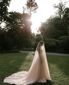 a woman in a wedding dress is standing on the grass with her back to the camera