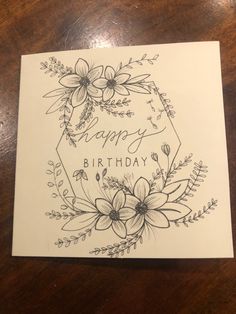 a happy birthday card with flowers and leaves on the front, sitting on a wooden table