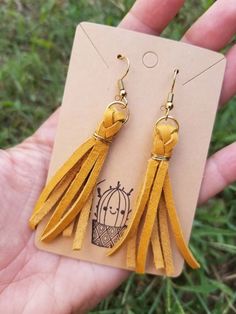 a pair of yellow leather tasseled earrings on a card in someone's hand