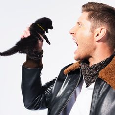 a man in a leather jacket is holding a small black kitten up to his face