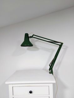 a green lamp is on top of a white table with a small drawer underneath it