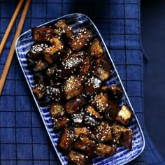 a blue and white plate topped with food next to chopsticks