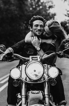 a man and woman are sitting on a motorcycle with their arms around each other's shoulders