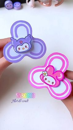 two hand holding small pink and purple flower brooches with hello kitty on them