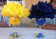 two wine glasses with flowers in them sitting on a table next to another glass filled with confetti