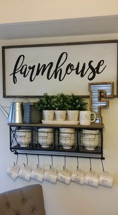 a sign that says farmhouse hangs on the wall above a shelf with cups and mugs