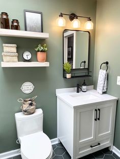 a white toilet sitting next to a bathroom sink under a mirror and light above it