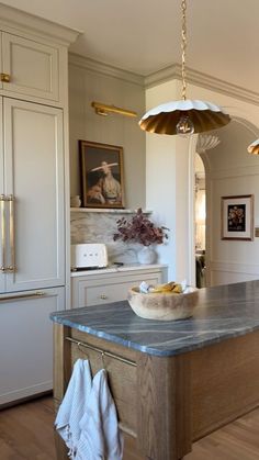 a large kitchen with an island in the middle and two hanging lights above it, along with white cabinets