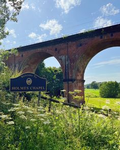 an old brick bridge with a sign in the foreground that says holmes chapel