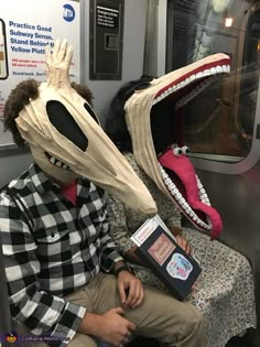 two people sitting on a train with masks on their heads and one wearing a fake alligator's mouth