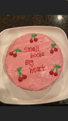 a pink cake sitting on top of a white plate covered in frosting and cherries