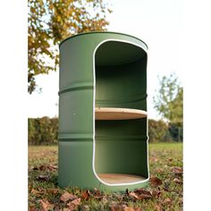 a green barrel sitting in the grass next to a tree with leaves on the ground