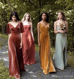 four women in long dresses standing next to each other on a dirt road with trees behind them