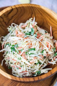 a wooden bowl filled with coleslaw and carrots on top of a table