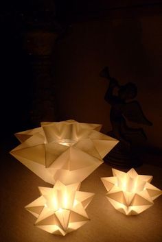 three white paper flowers sitting on top of a table next to a vase with candles in it