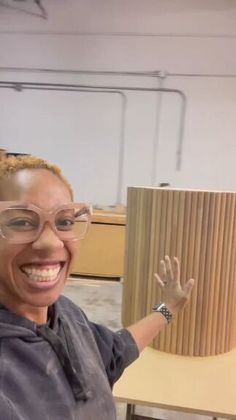 a woman in glasses is smiling and holding up a large wooden object with her hands