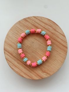 a bracelet with pink, blue and green beads on a wooden stand in front of a white background