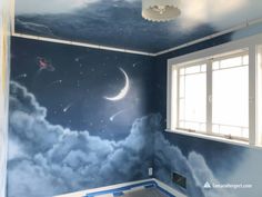 an empty room with blue walls and clouds painted on the wall, there is a window in the corner