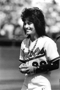 a black and white photo of a woman in baseball uniform holding a tennis racket