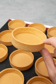 a hand is picking up some cake from a pan on a baking tray filled with cupcakes