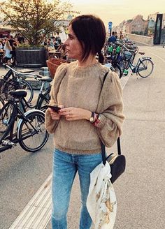 a woman is standing on the sidewalk looking at her cell phone and holding a purse