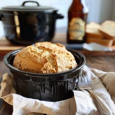 a loaf of bread sitting in a black bowl on top of a wooden table next to a bottle of beer