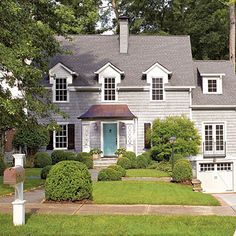 a gray house with white trim and black shutters on the front door is surrounded by lush green trees