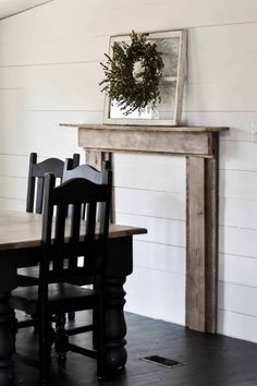 a dining room table with chairs and a wreath on top of the fireplace mantel