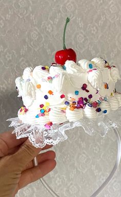 a hand holding a cake with white frosting and sprinkles on it