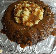 a piece of meat covered in gravy and mashed potatoes on aluminum foil