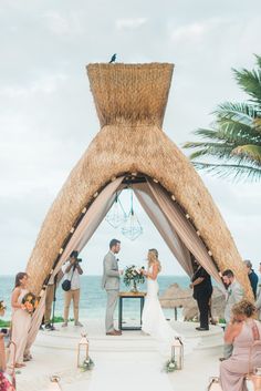 a couple getting married on the beach in front of some palm trees and people standing around