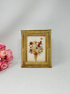 a bouquet of flowers sitting in front of a framed picture on a white background next to pink roses