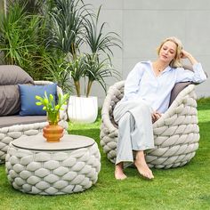 a woman sitting in a chair next to a table and potted plant on the grass