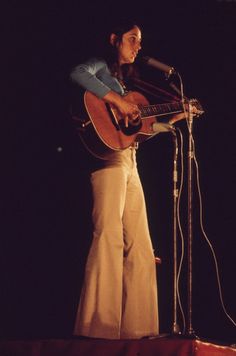 a woman standing in front of a microphone while holding a guitar