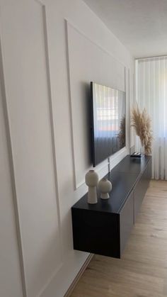 a flat screen tv sitting on top of a black shelf in a living room next to a window